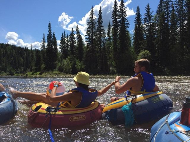 Two people tubing on Pembina River with trees in the background