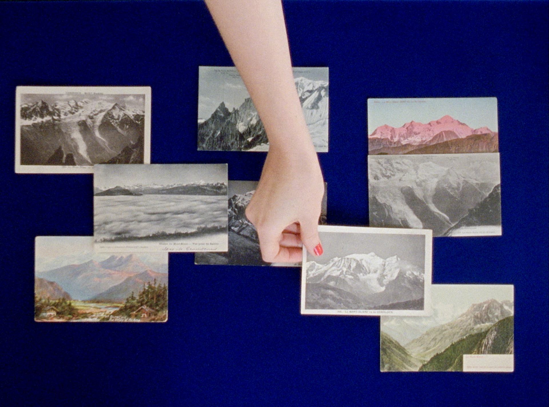 Hand holding mountain photo with others scattered on blue background.