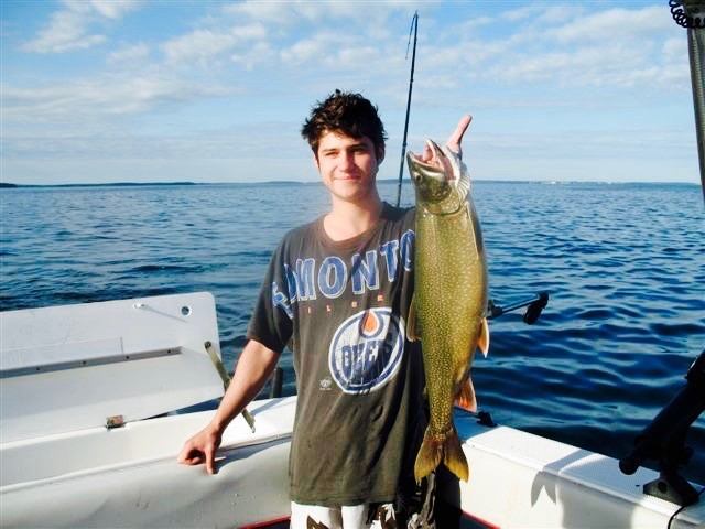 Young angler proudly shows off a big catch aboard a fishing boat on a calm, sunny lake day.