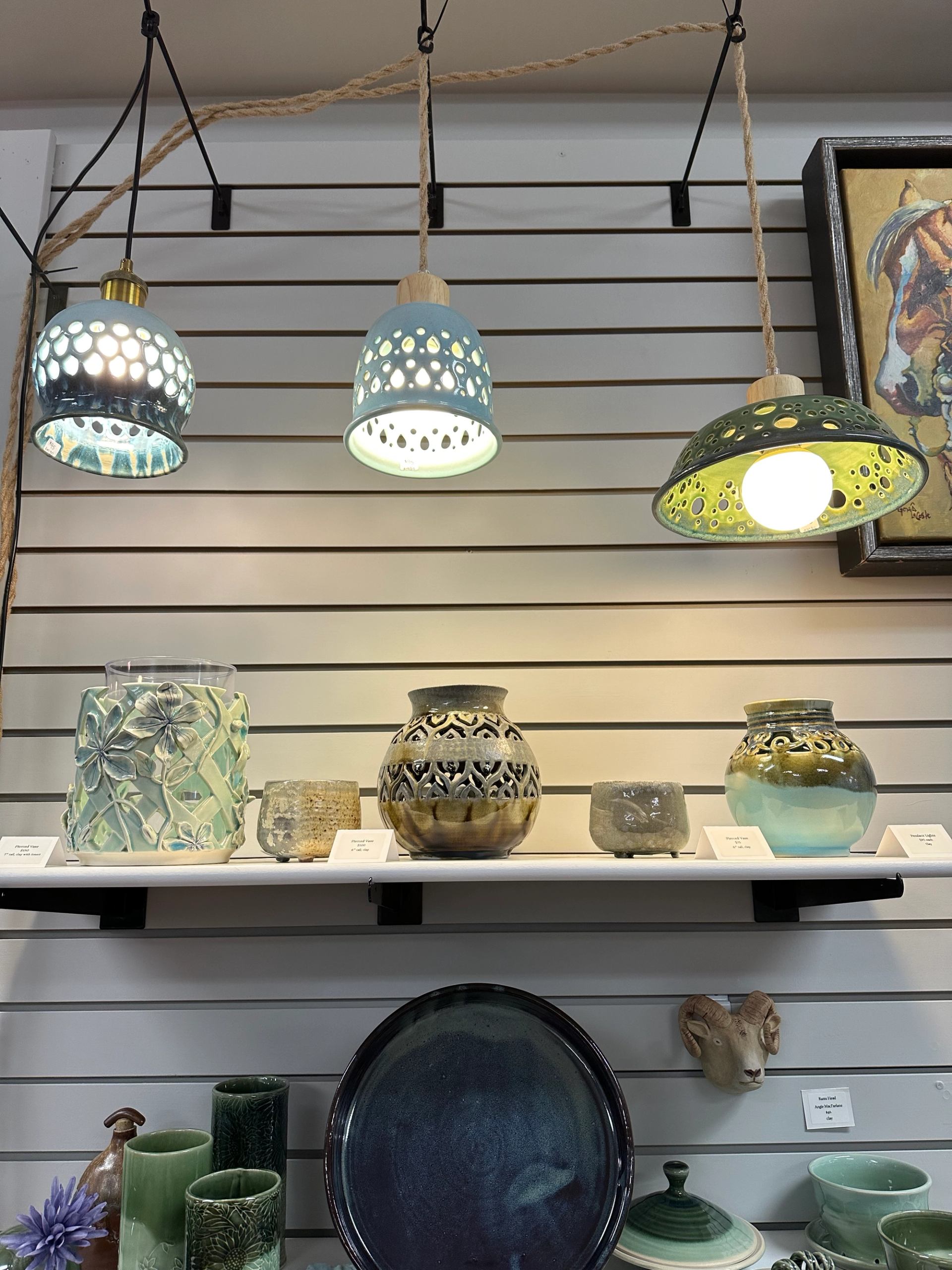 Ceramic vases, bowls, and hanging lights arranged on shelves in a gallery.