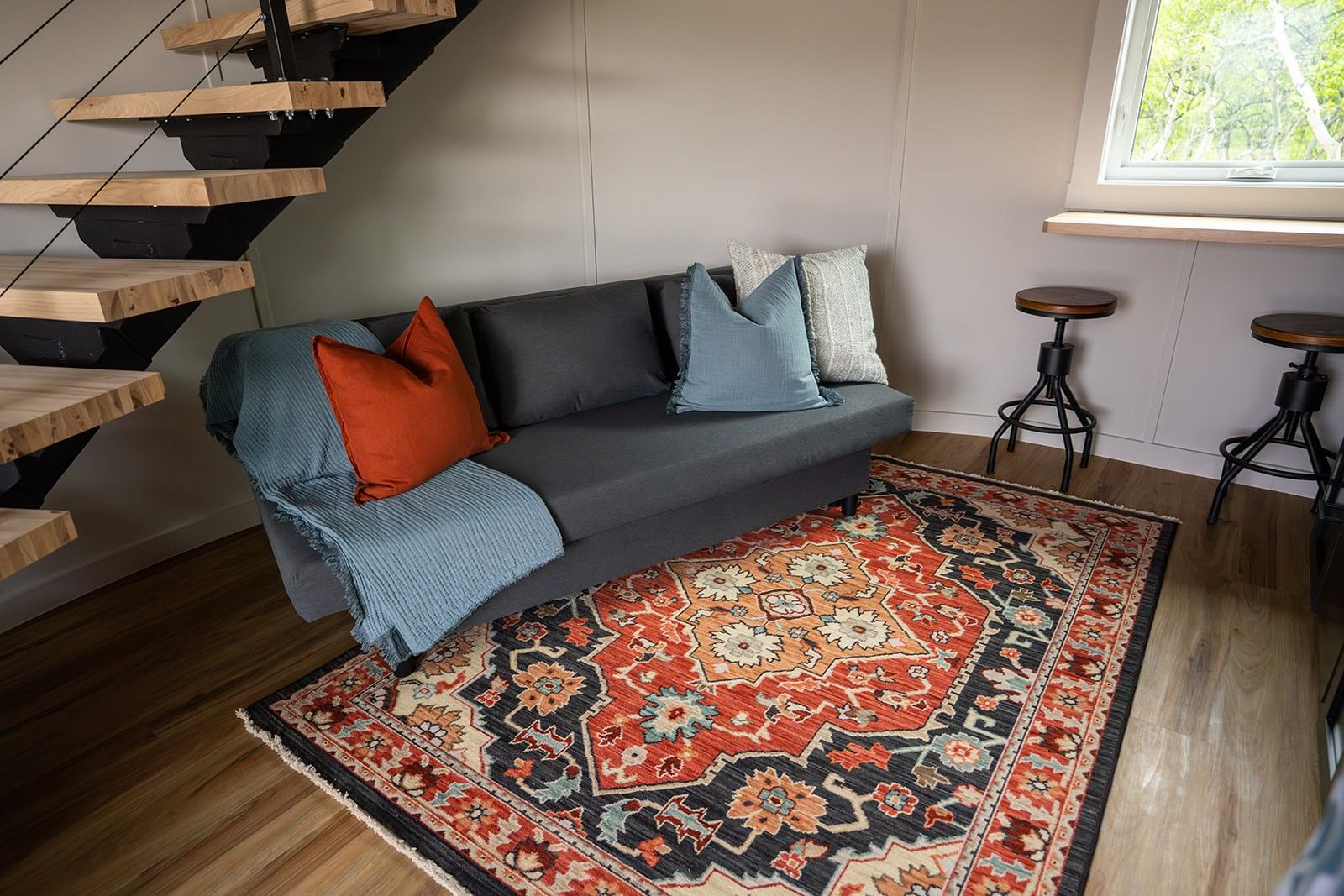 Twin Butte Silos living area with gray sofa, colorful rug, and modern staircase.