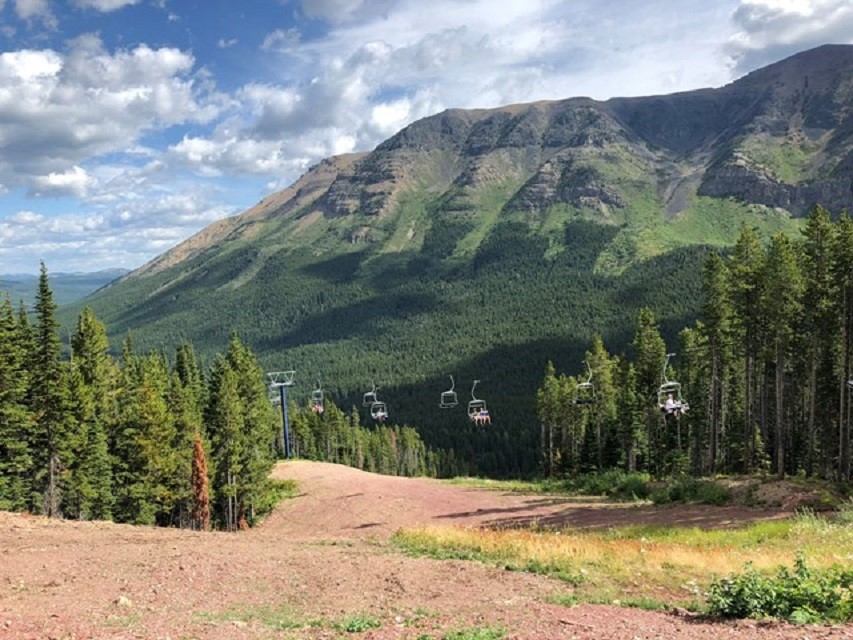 Mountain ski hill with empty chairlifts above forested slopes under partly cloudy sky.
