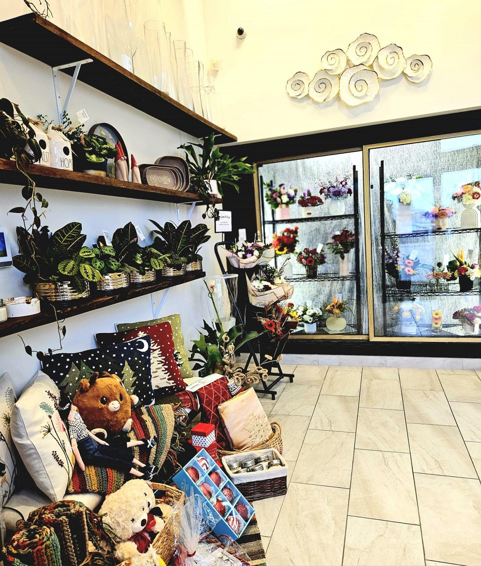 Store interior with plants, pillows, and floral arrangements in glass case.