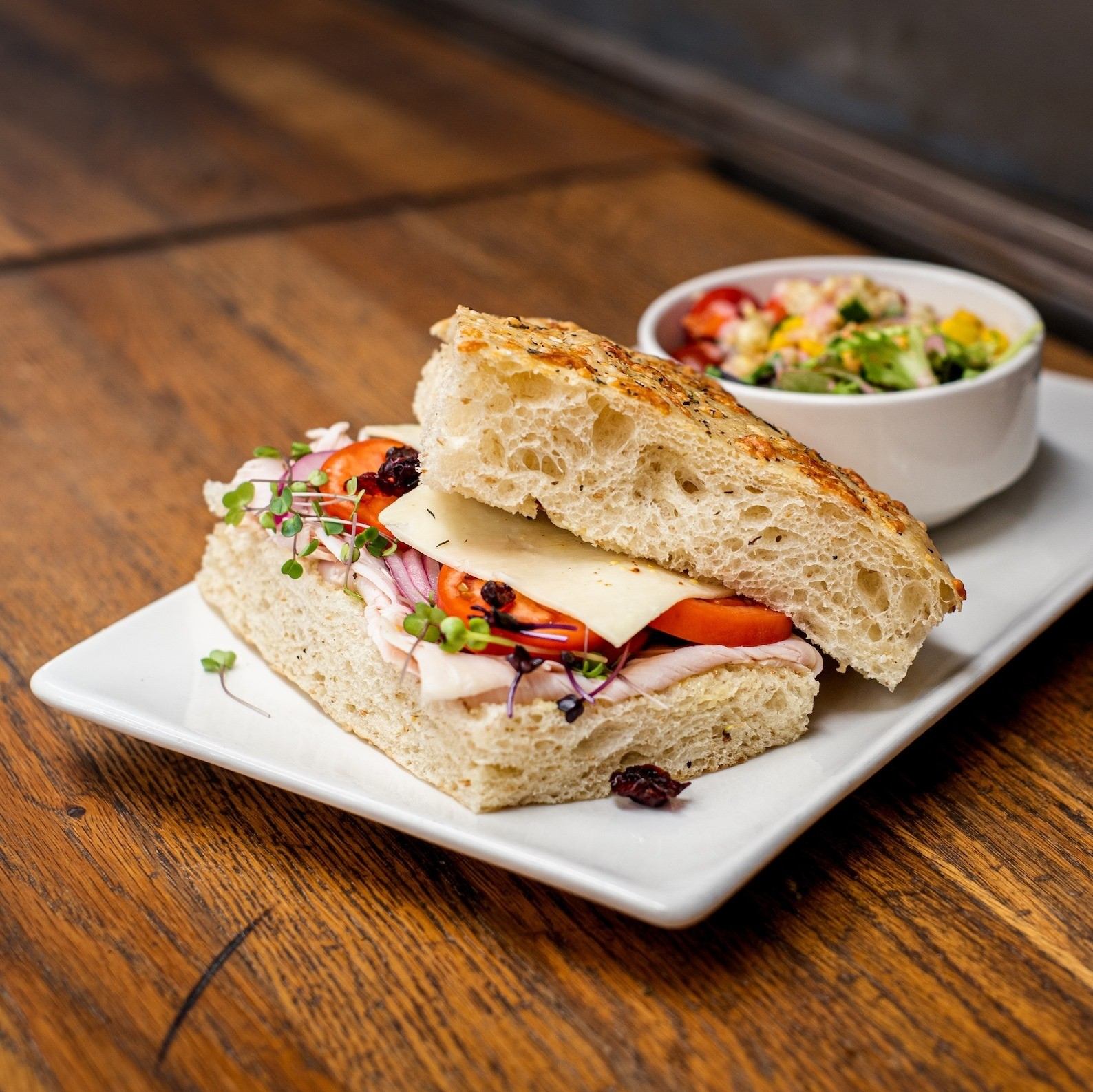 Gourmet sandwich on focaccia served with fresh salad on a white plate.
