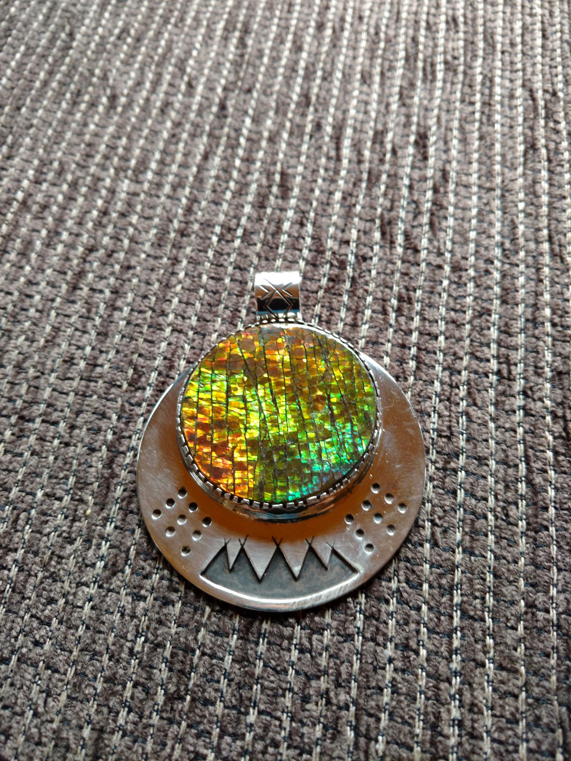 Iridescent gemstone pendant with engraved metal on fabric background.