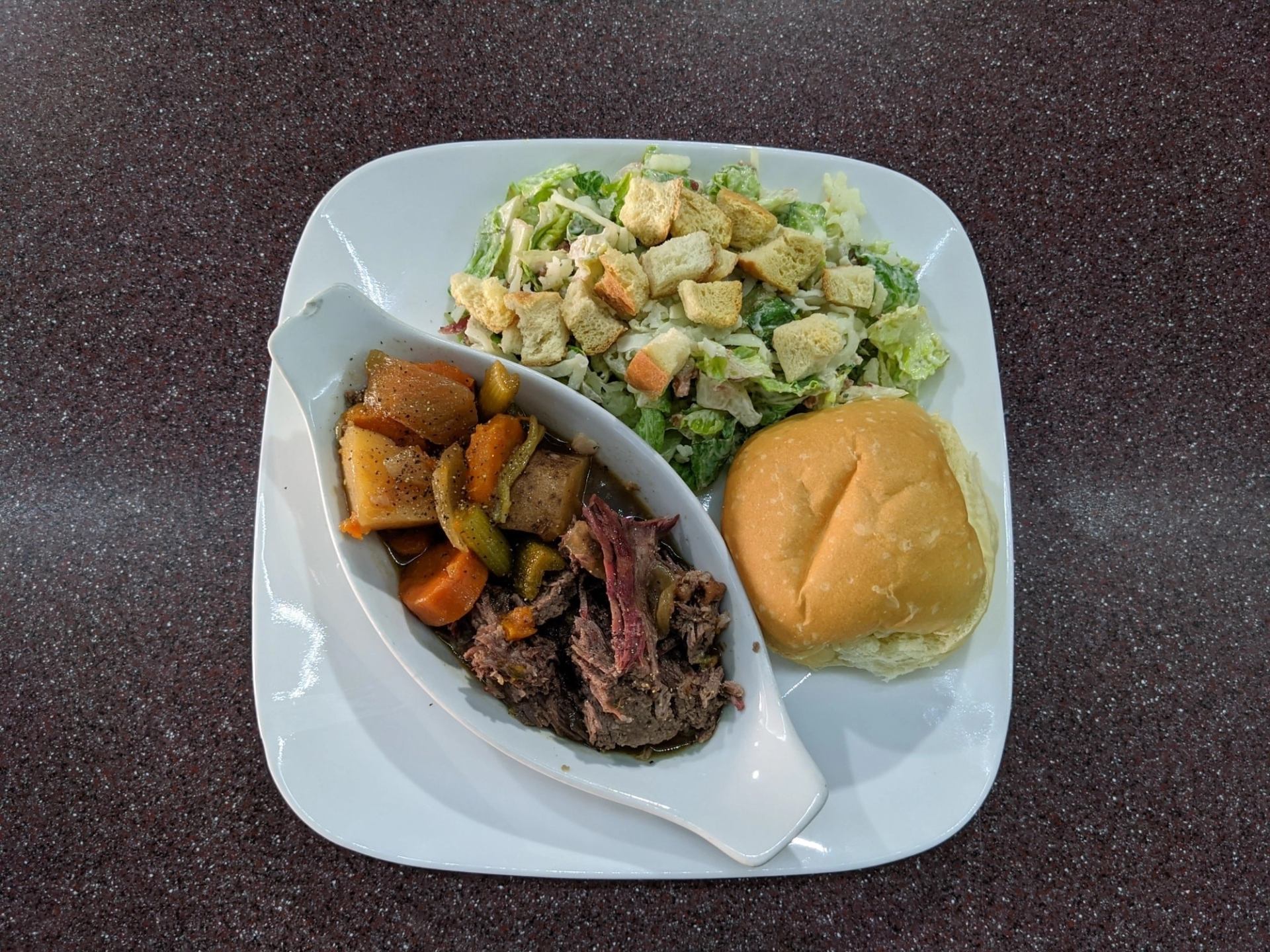 Plate with pot roast and vegetables, Caesar salad with croutons, and a dinner roll.
