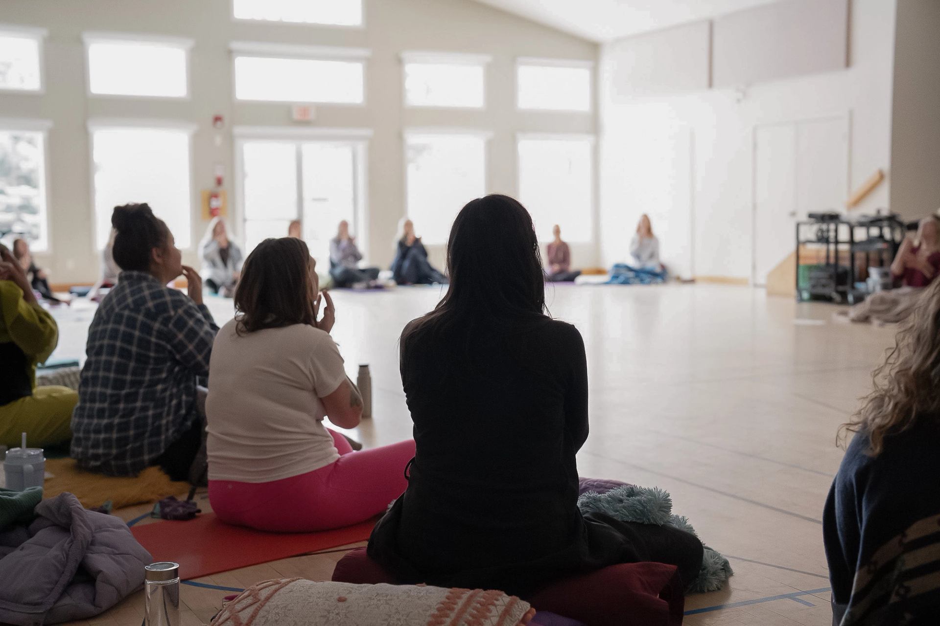People sit on cushions in a bright studio, facing a circle of others.