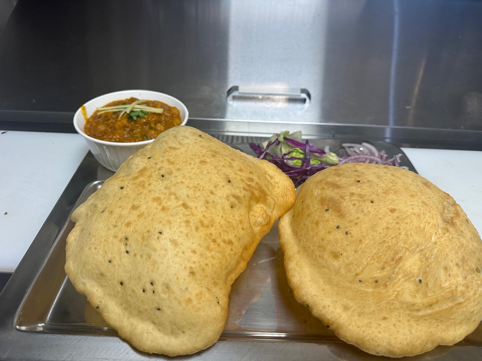 Fried Indian bread with curry, onions, and chilies on a metal tray.