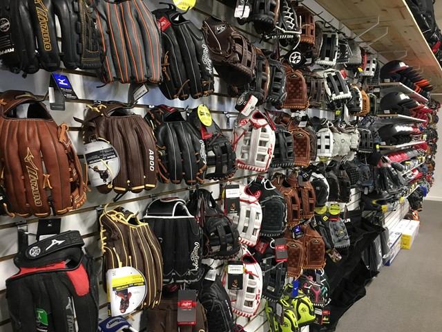Wall display of baseball gloves and sports bags with price tags in a store aisle.