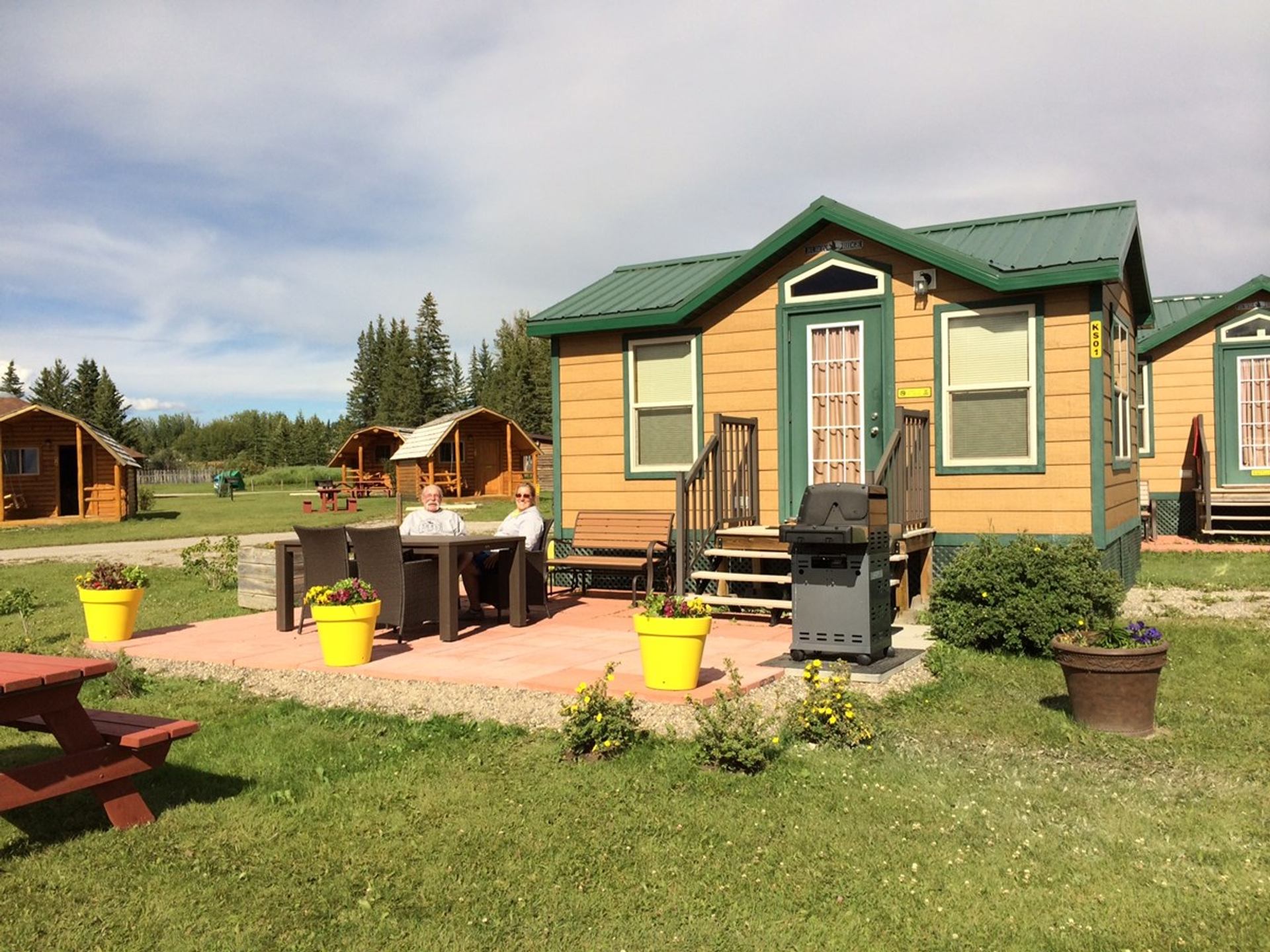Campground cabins with covered porches sit among grassy sites beneath a bright open sky landscape.