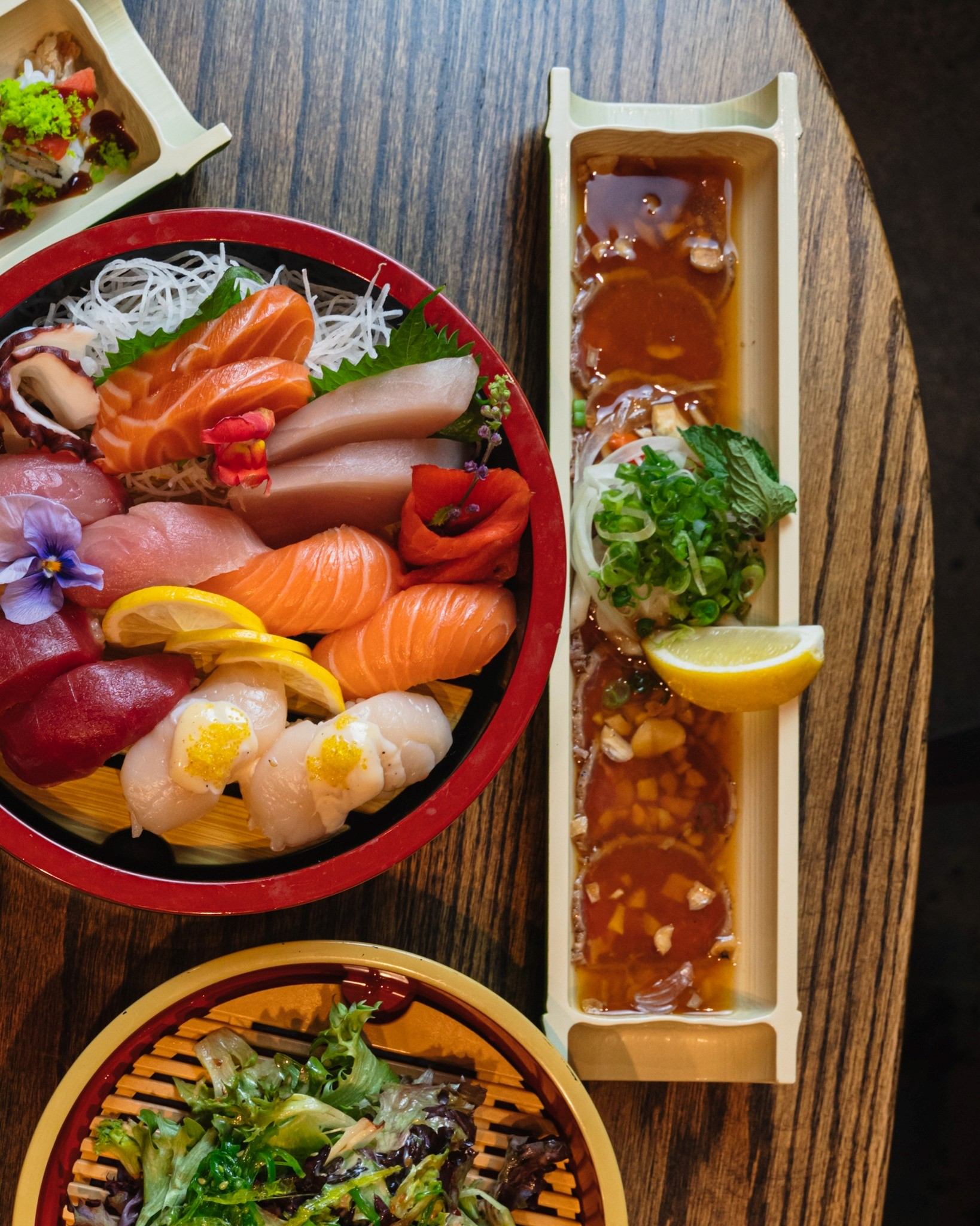 Sashimi bowl and sushi rolls with sauce and lemon, on a wooden table.