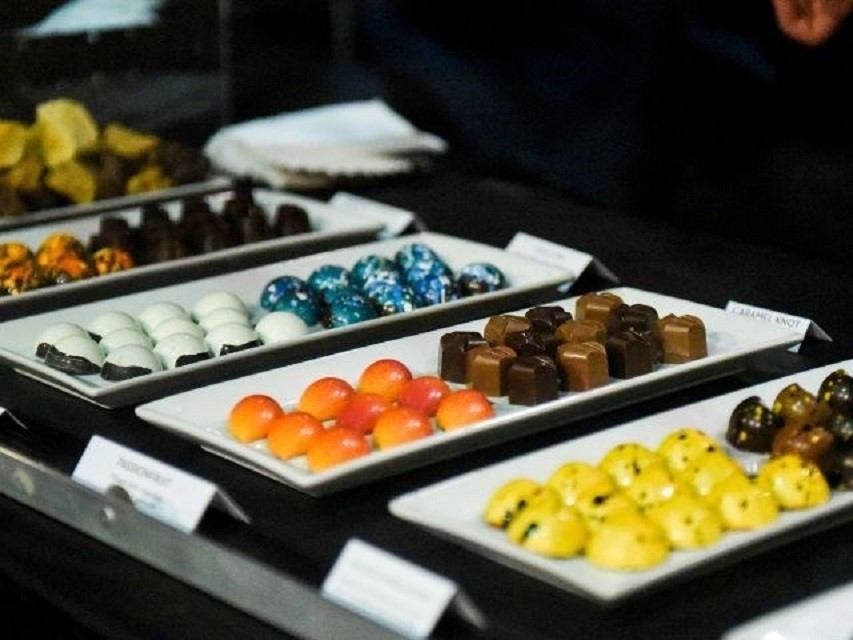 Assorted colourful chocolates arranged on white trays at a display table with labels.