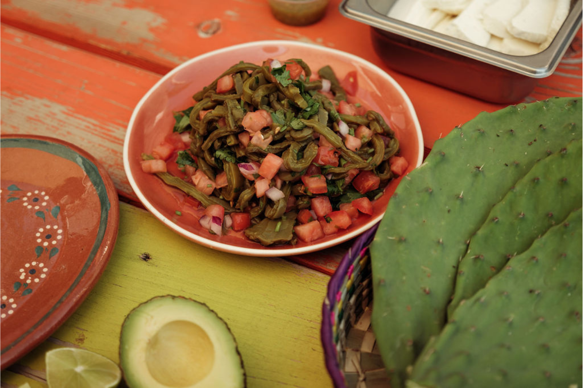 Colorful plate of nopales with avocado, lime, and festive decor on wooden surface.