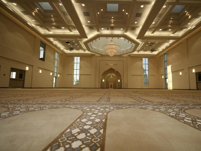 Spacious prayer hall inside Baitun Nur Mosque with patterned carpet, chandelier, and arched details.