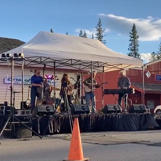Outdoor live band performs on stage under white event tent, with instruments and speakers.