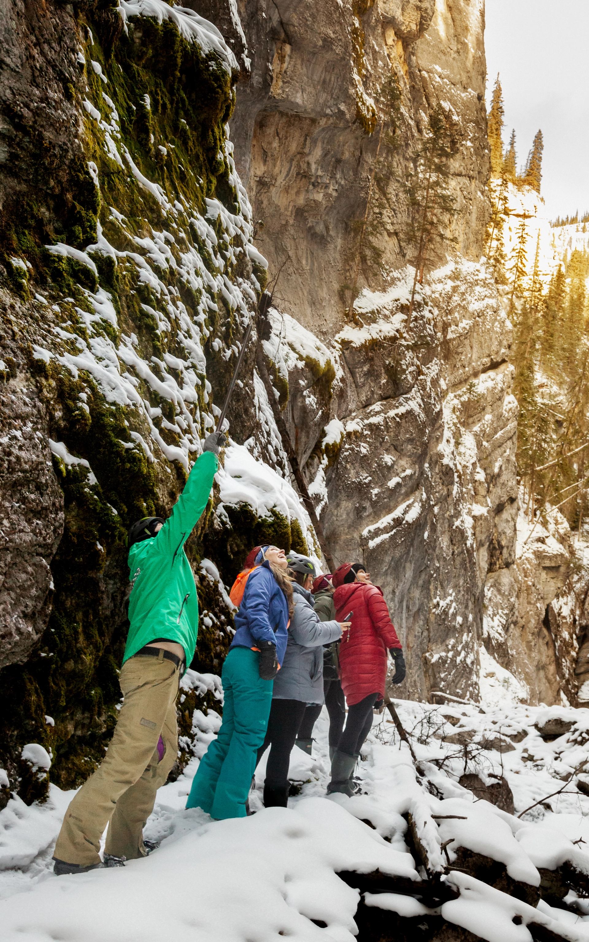A group walks along a snowy canyon floor beside steep rock walls during a winter icewalk.