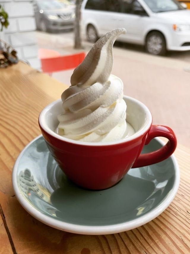 Red cup on a saucer filled with swirled vanilla soft‑serve on a café table.