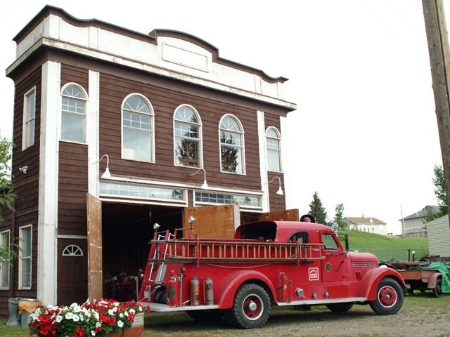 Vintage red fire truck outside historic fire station with arched windows and flowers.