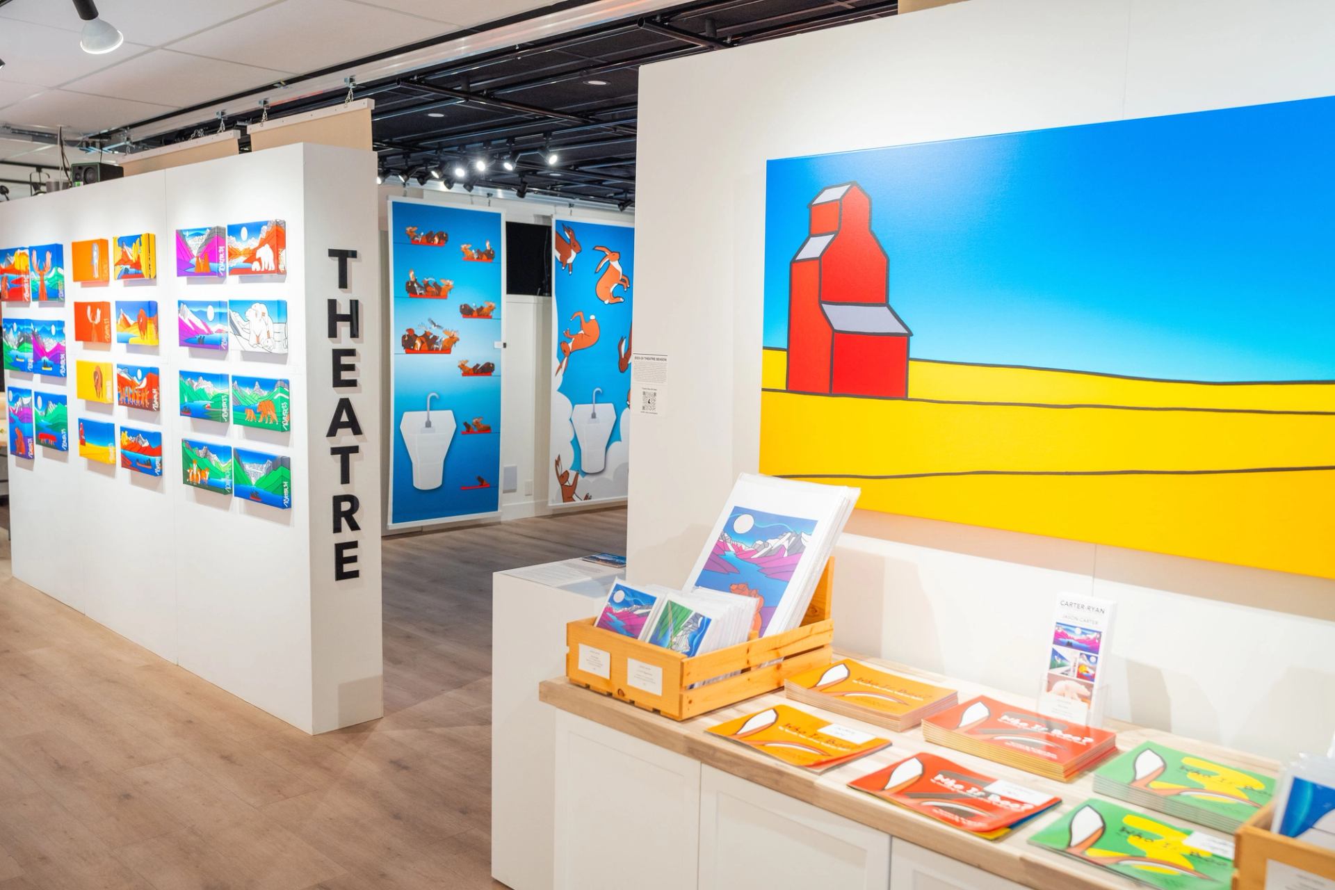 Bright gallery interior with colourful graphic paintings and prints displayed on white walls.