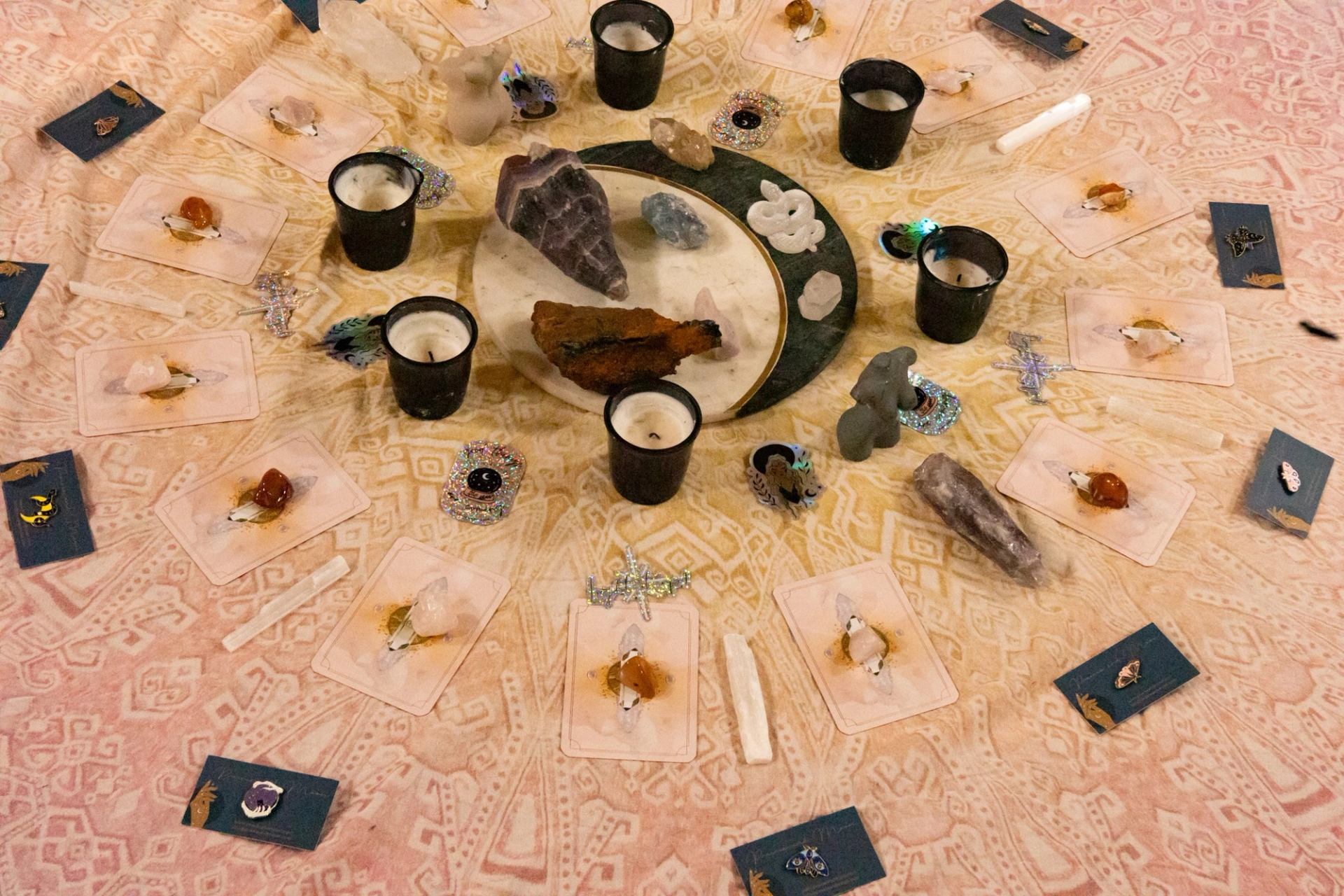 Circular altar arrangement with crystals, tarot cards, tealight candles and small decorative objects.