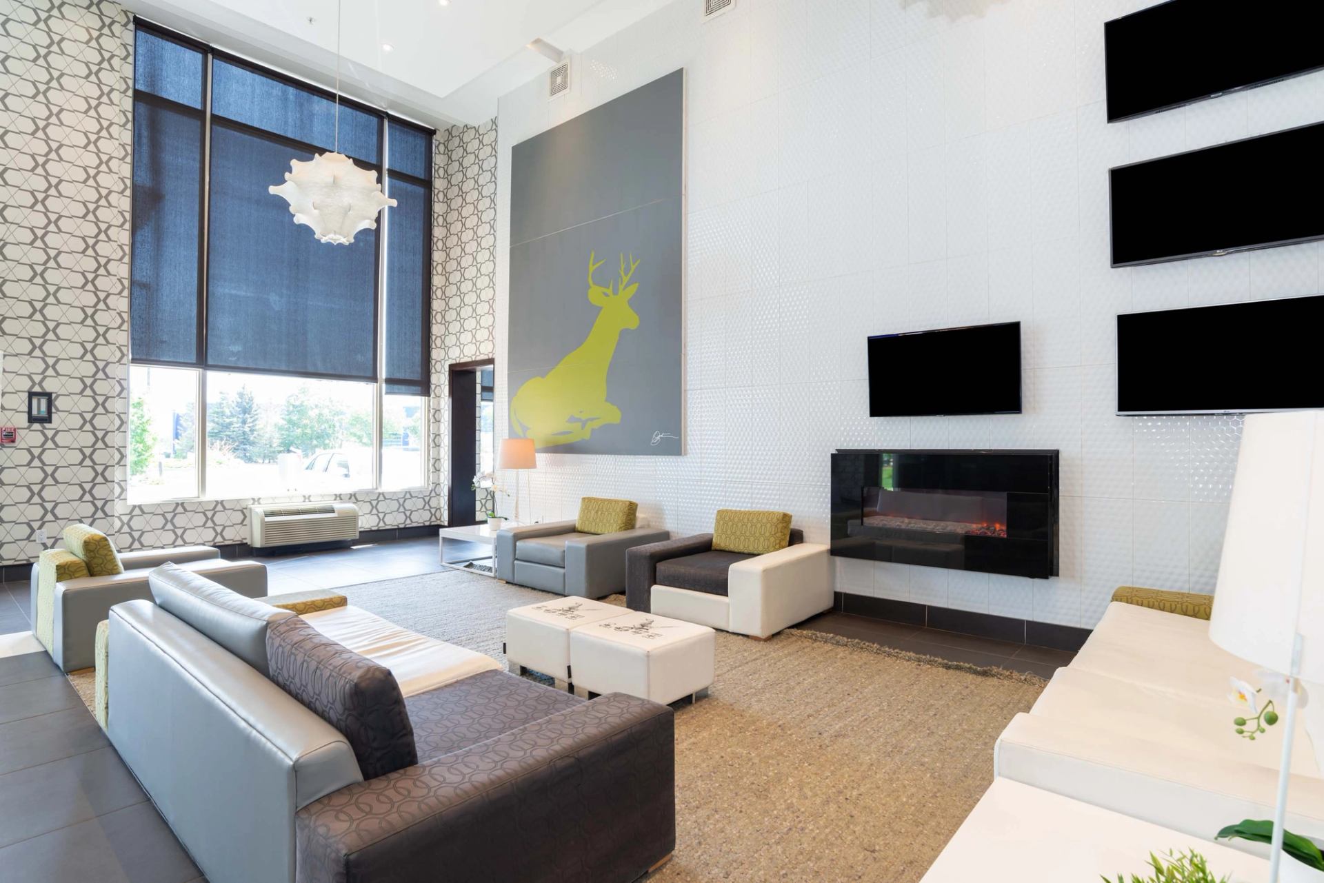 Modern lobby with sofas, large deer artwork, fireplace and tall windows with blinds.