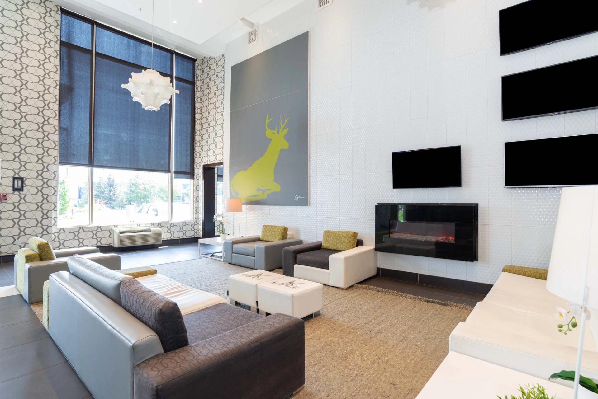 Modern lobby with sofas, large deer artwork, fireplace and tall windows with blinds.