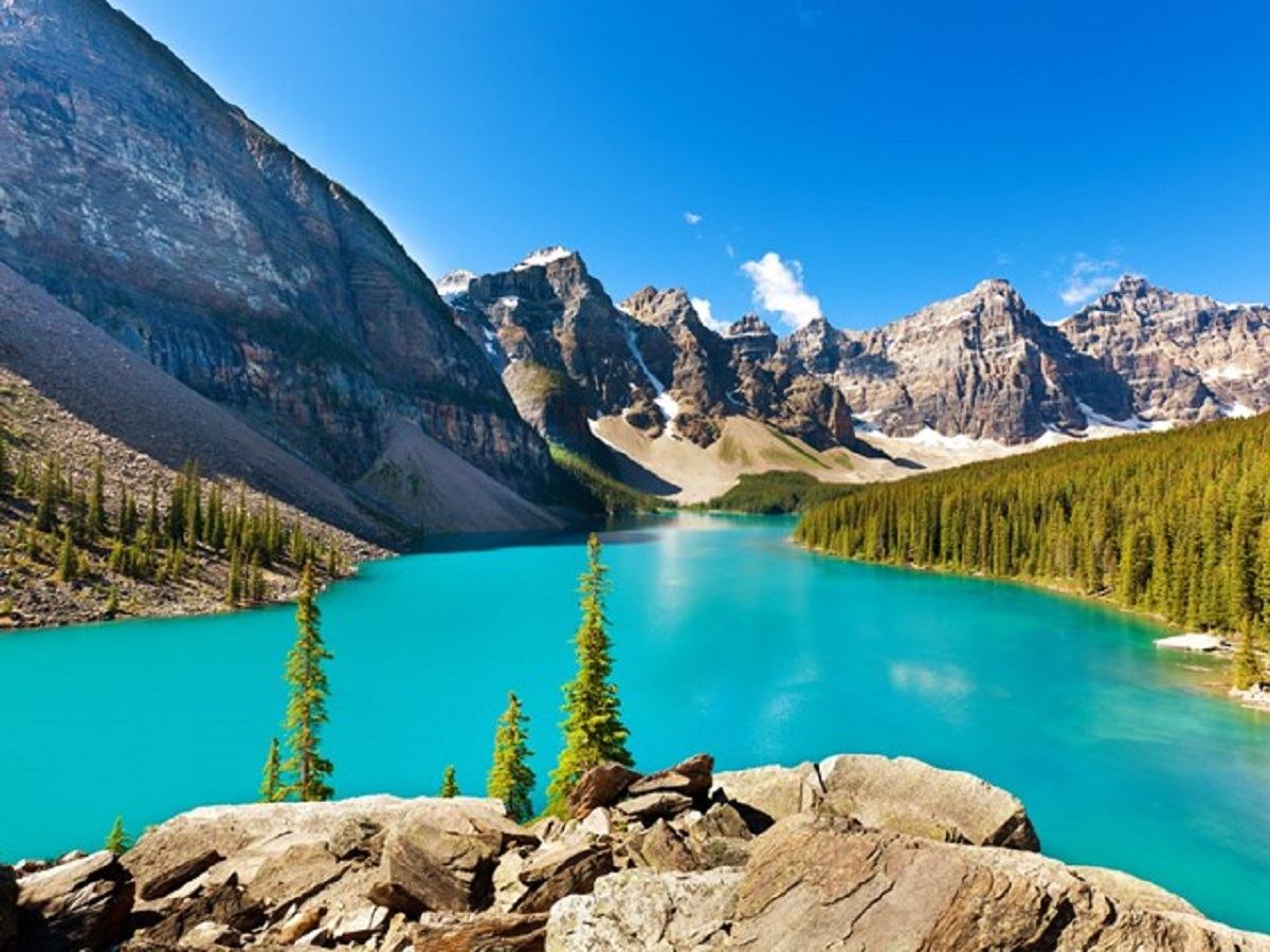 A bright turquoise lake surrounded by steep rocky peaks and evergreen trees.