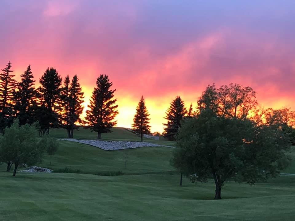 Golf course fairway with trees under a colorful sunset sky.