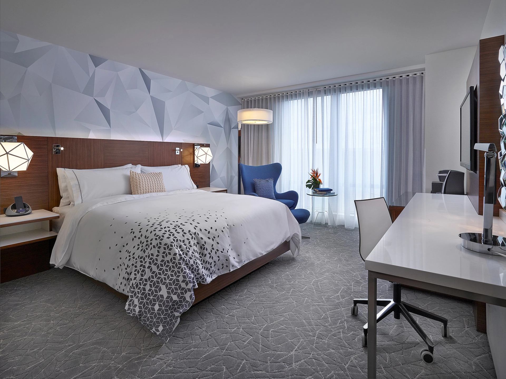 Stylish hotel room with king bed, desk, and blue armchair.