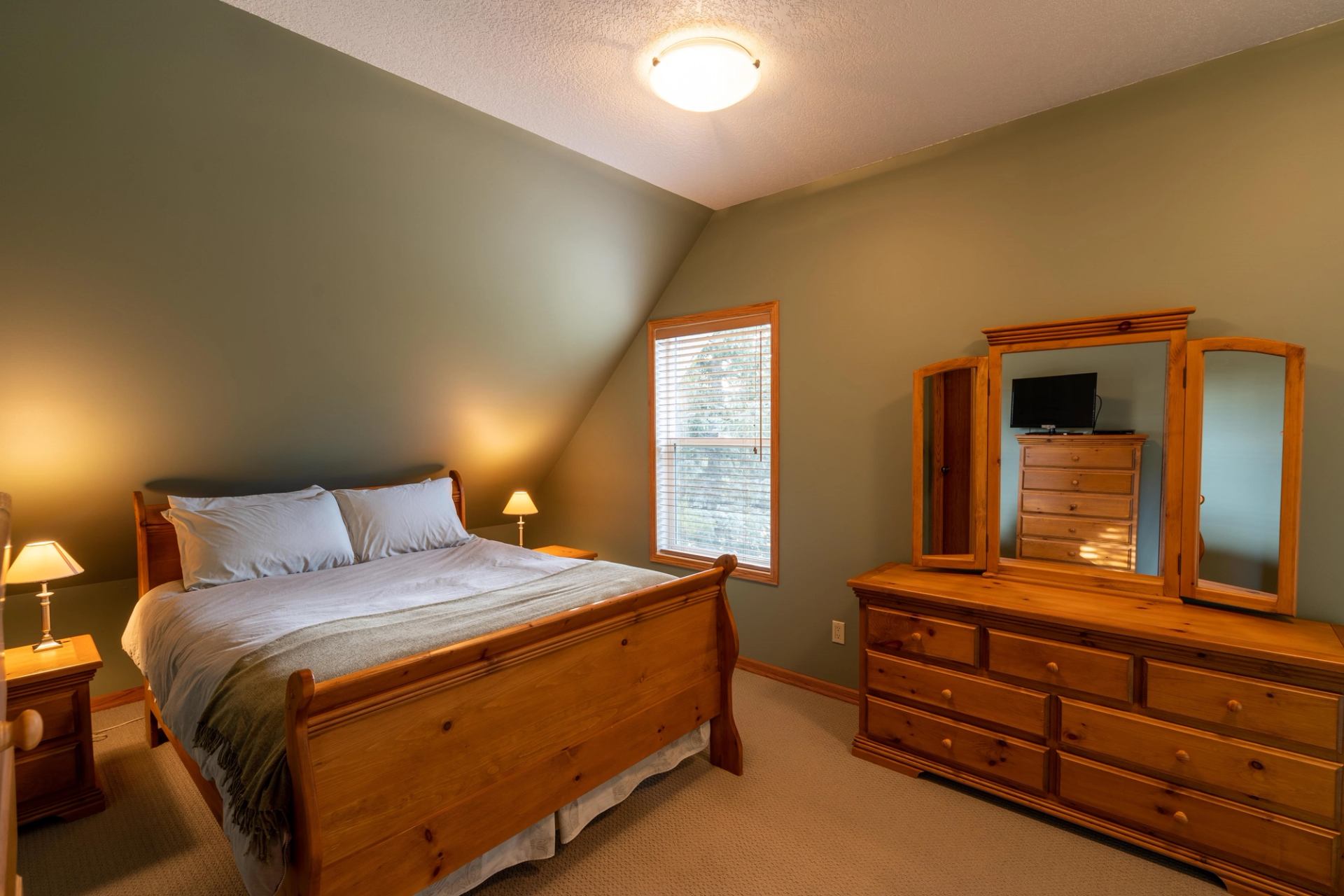 Bedroom with double bed, dresser, mirror cabinet, and window with blinds.