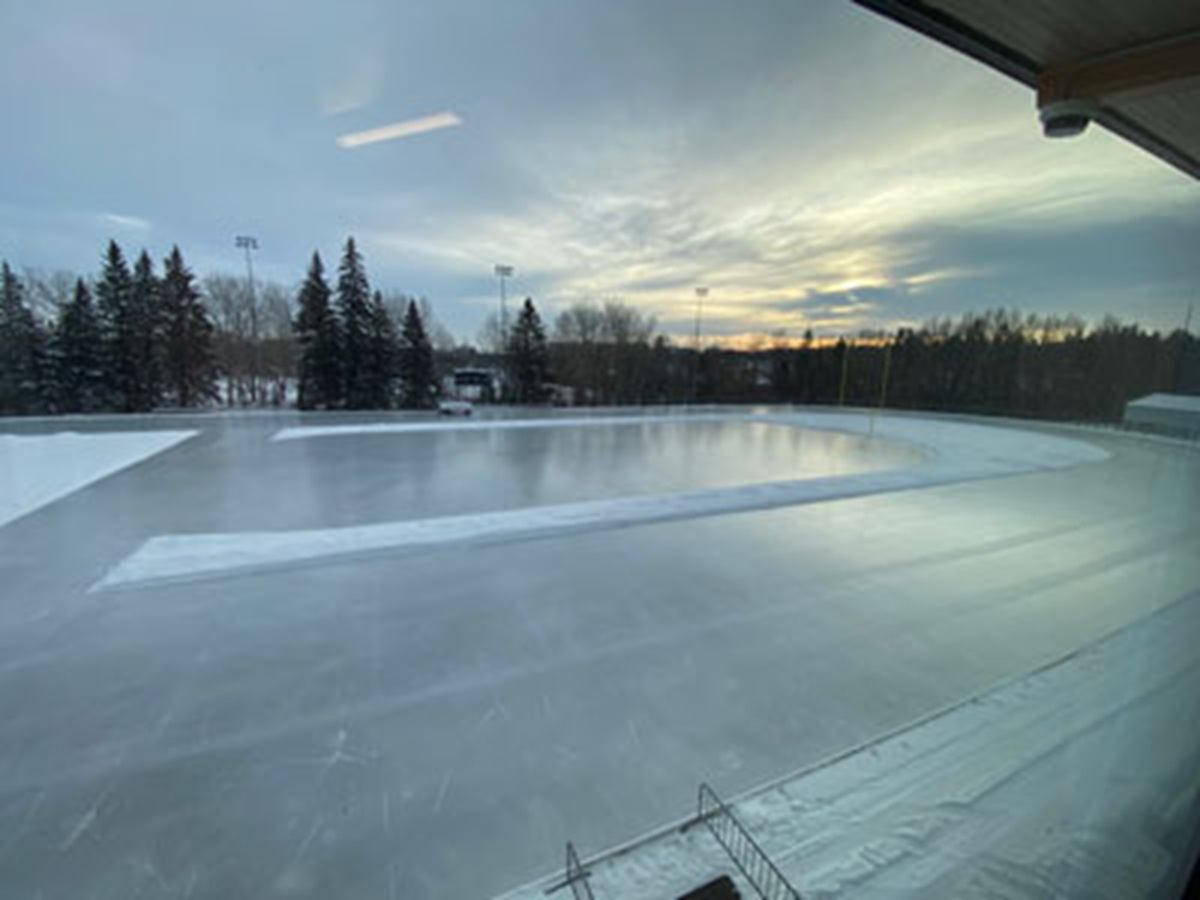 Outdoor ice track with surrounding snow, trees and light poles under cloudy sky.