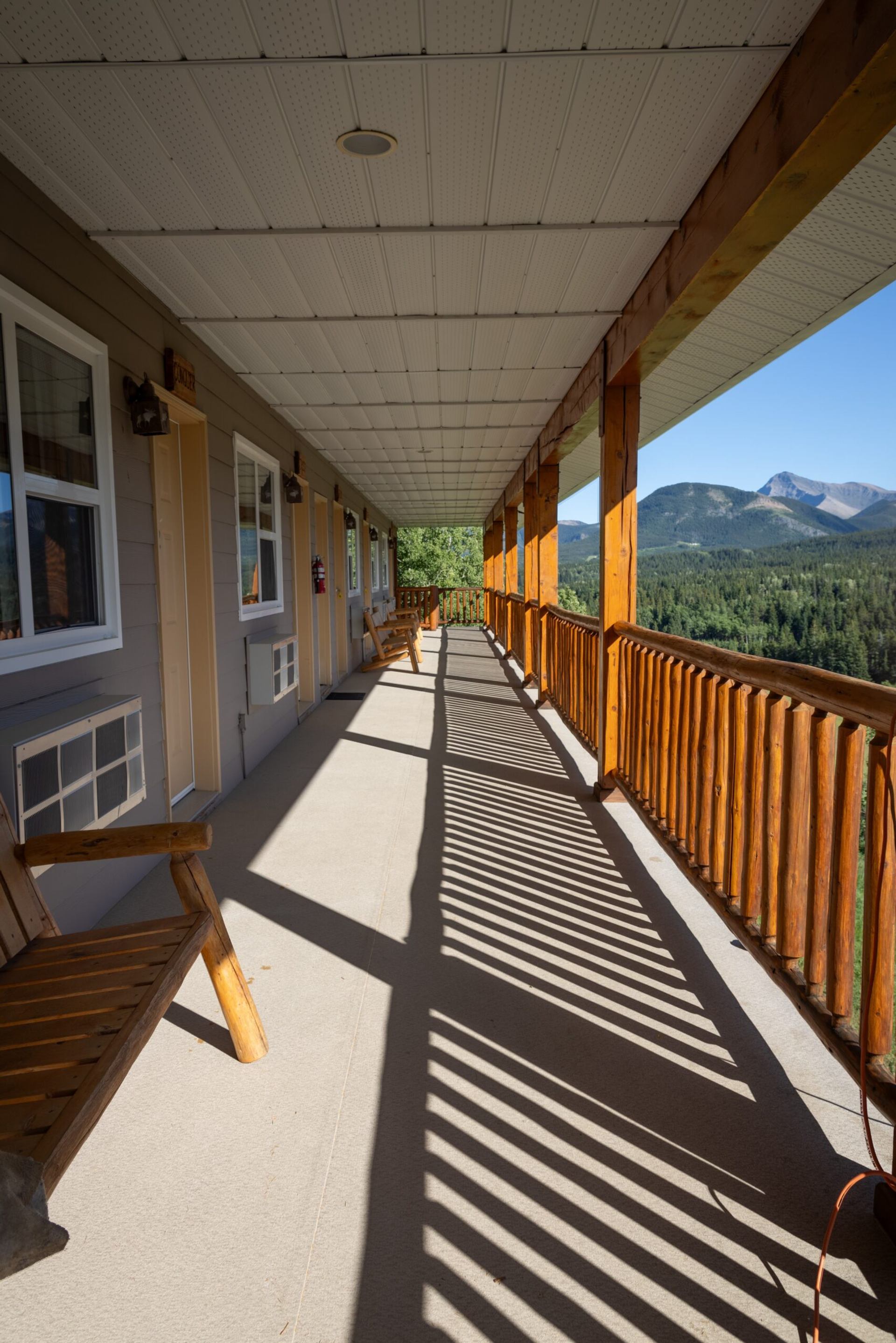Wooden chairs along a covered ranch walkway with forest and mountain views.