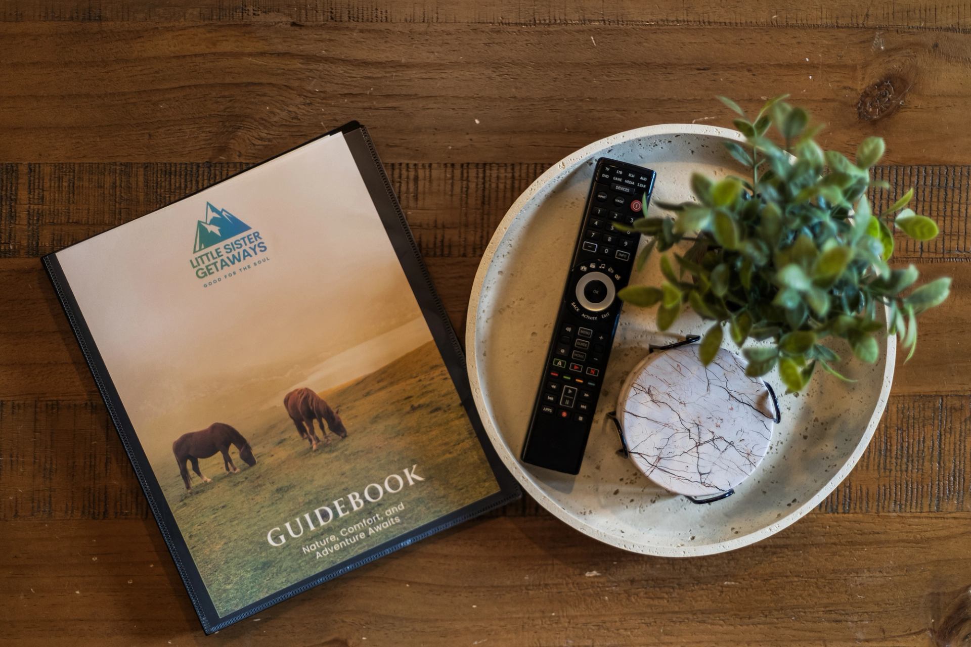 Little Sister Getaways guidebook beside a tray with a plant, remote and coasters.