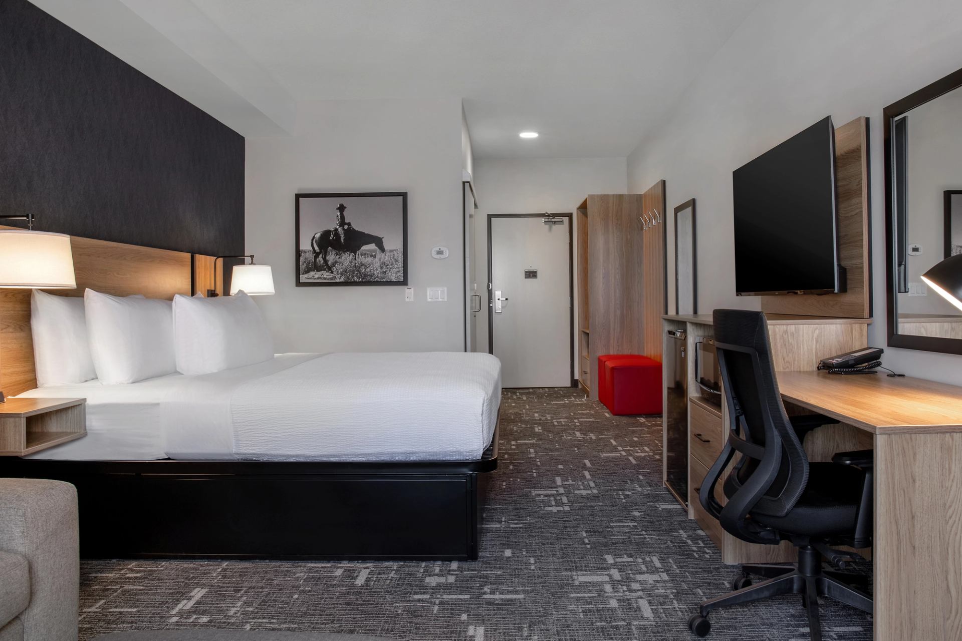 Hotel room with king bed, desk, wall-mounted TV and cowboy artwork above headboard.