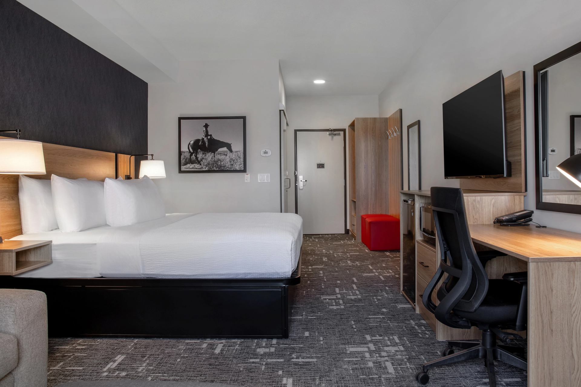 Hotel room with king bed, desk, wall-mounted TV and cowboy artwork above headboard.