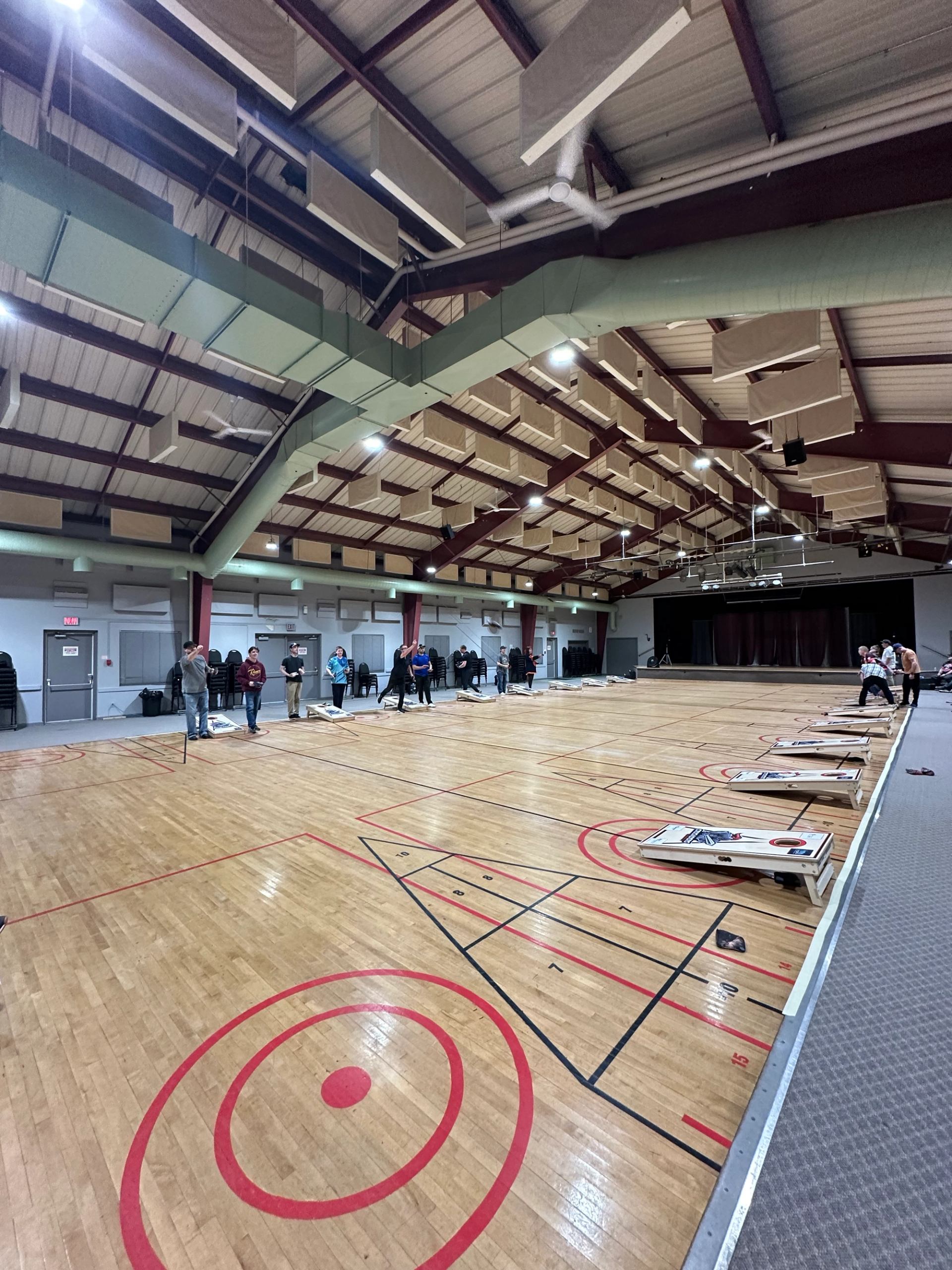 Wide view of a gym filled with cornhole boards and participants