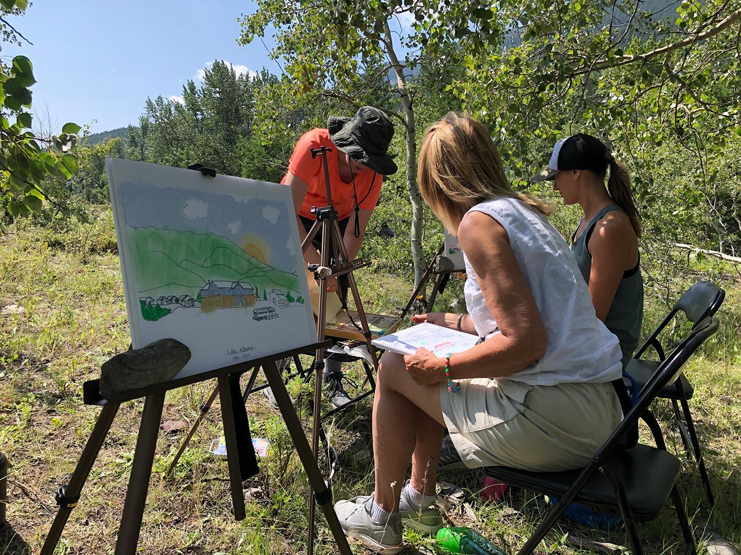 People painting on easels in a shaded forest clearing.