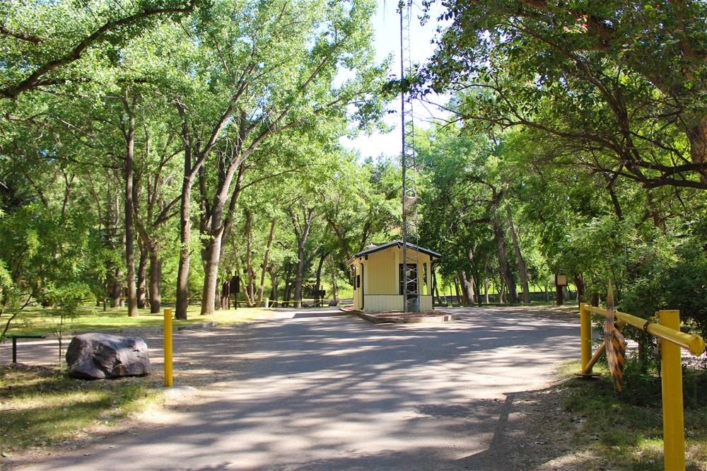 Entrance booth at Taber Municipal Park surrounded by tall green trees and a paved road.