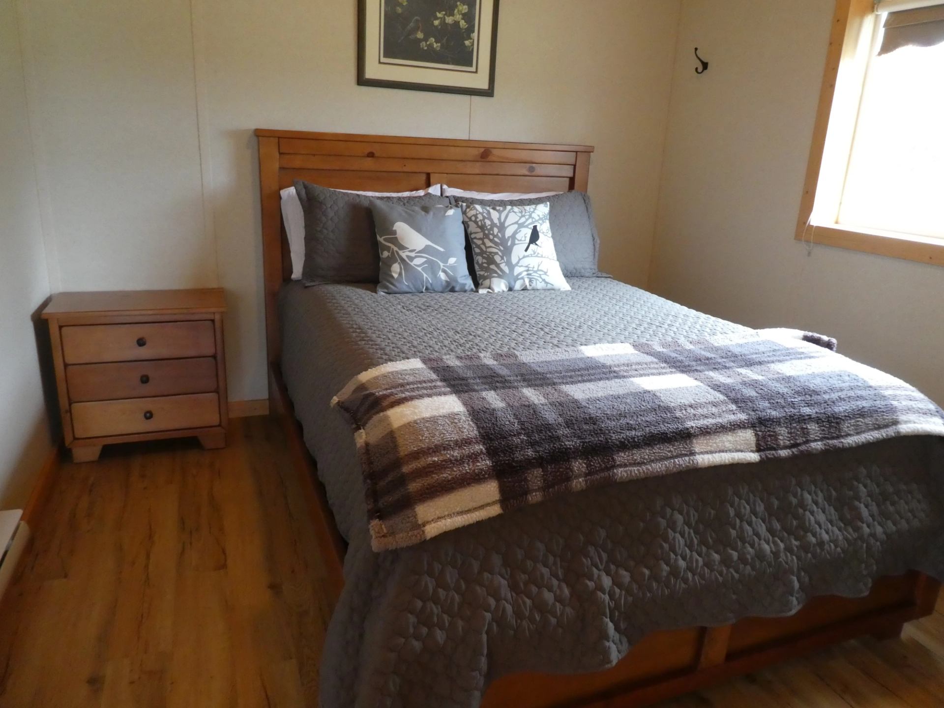 Peace River Cabins bedroom with wooden bed, plaid blanket, and nightstand.