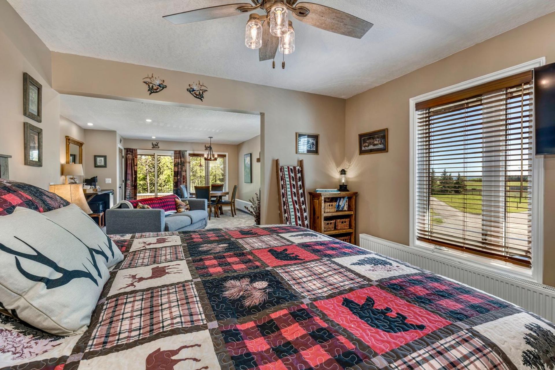 Bedroom with patchwork quilt, ceiling fan, and view into open living and dining area.