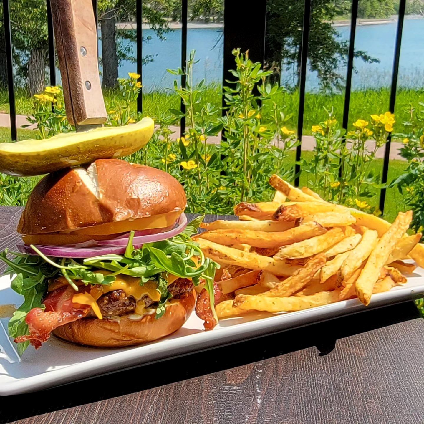 Burger and fries served outdoors with lake view and garden setting.