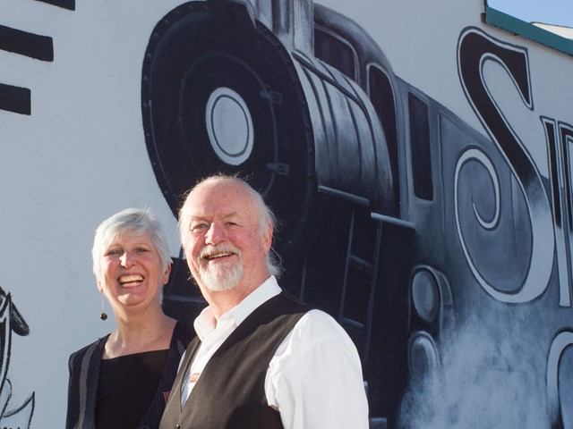 Two people standing in front of train mural on a wall.