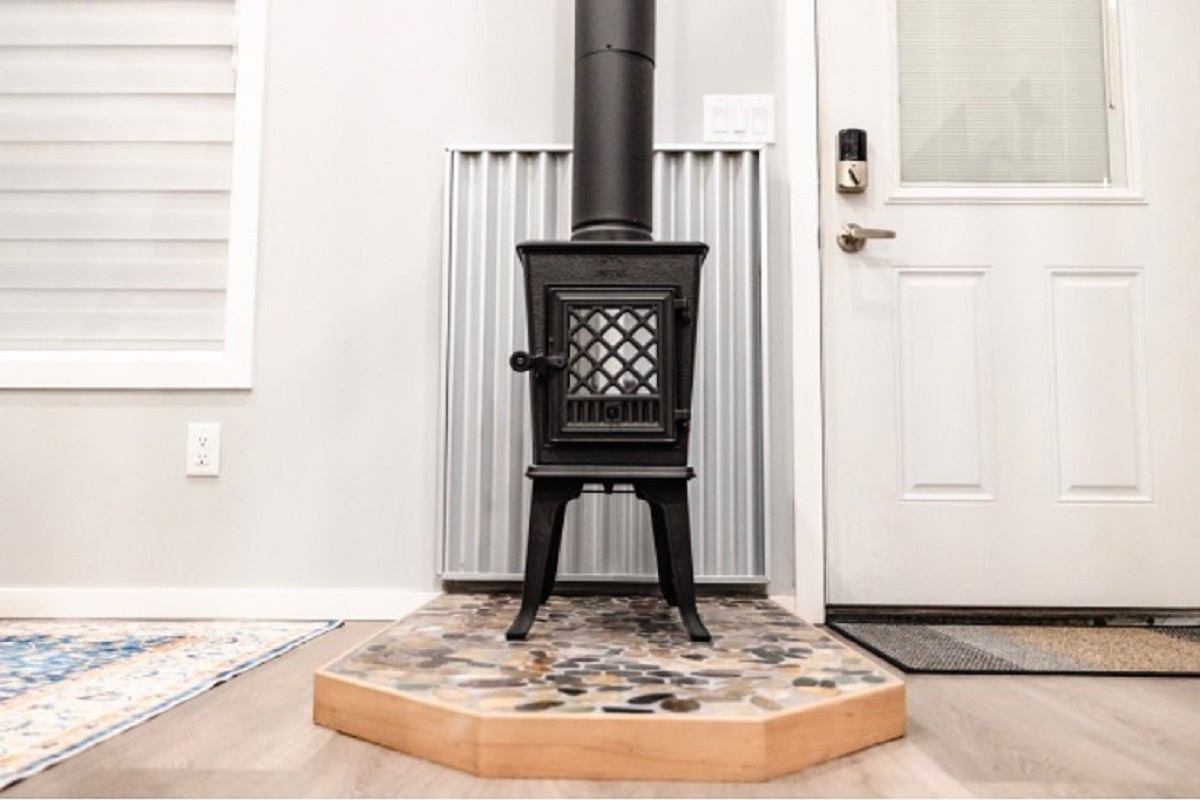 Small black wood‑burning stove on a stone hearth inside a bright bungalow entryway.