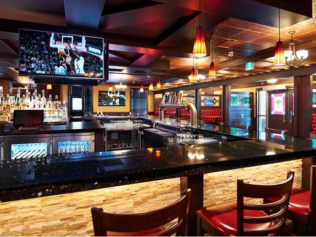 Bar interior with red chairs, granite counter, and TV showing basketball.