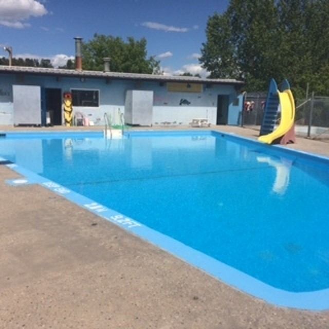 Outdoor swimming pool with blue water, poolside deck, and yellow and blue slides.