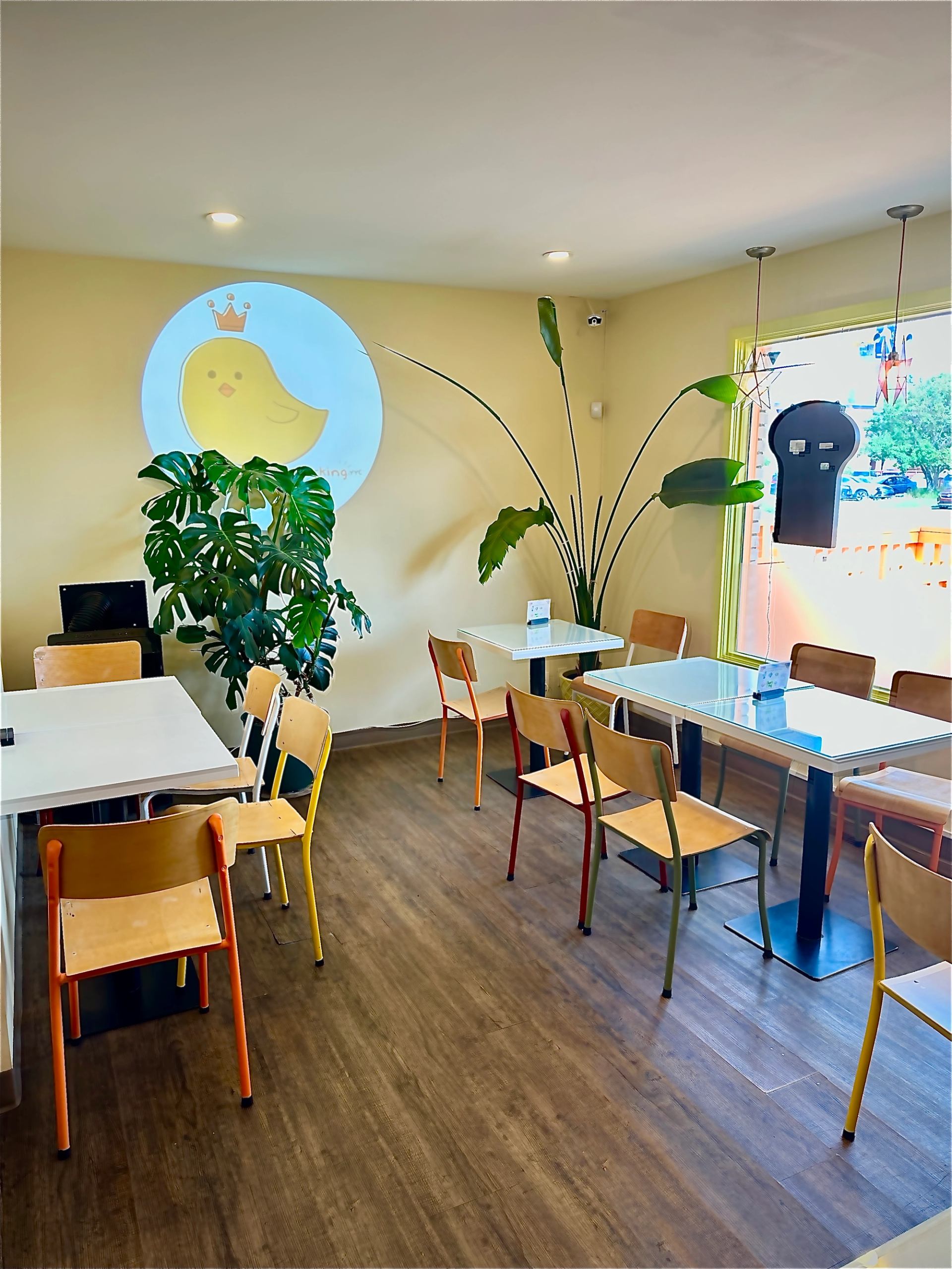 Dining area with colourful chairs, white tables, large plants and a chick mural.