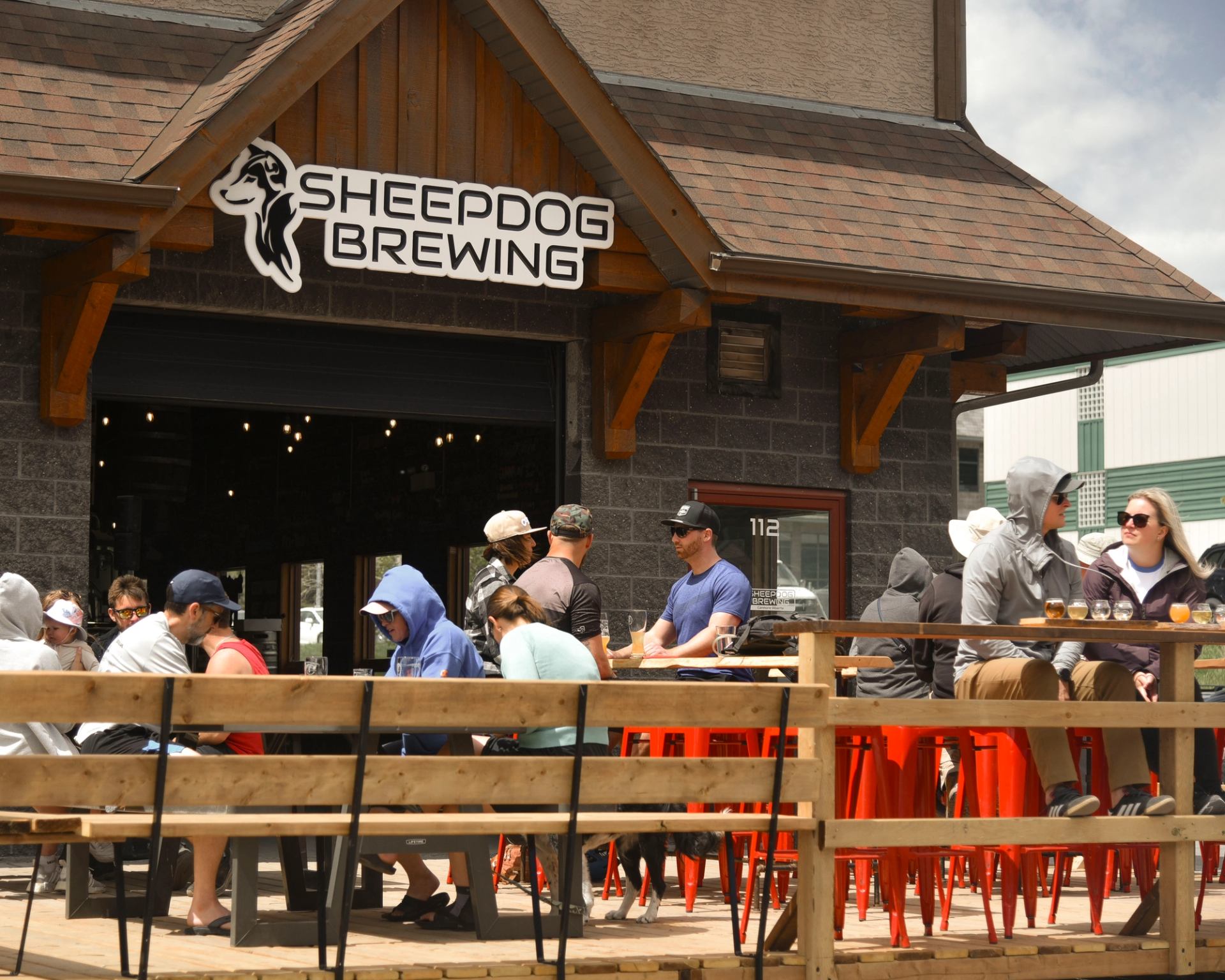 Patrons sit at outdoor tables beneath the Sheepdog Brewing sign.