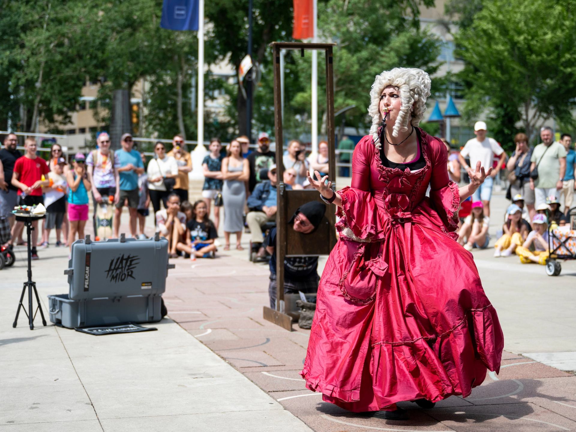 Street performer in red historical dress entertains gathered crowd in outdoor public square.