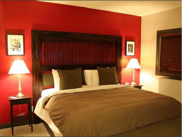 Warm bedroom with bold red accent wall and dark wood headboard at Smoky Lake Inn.