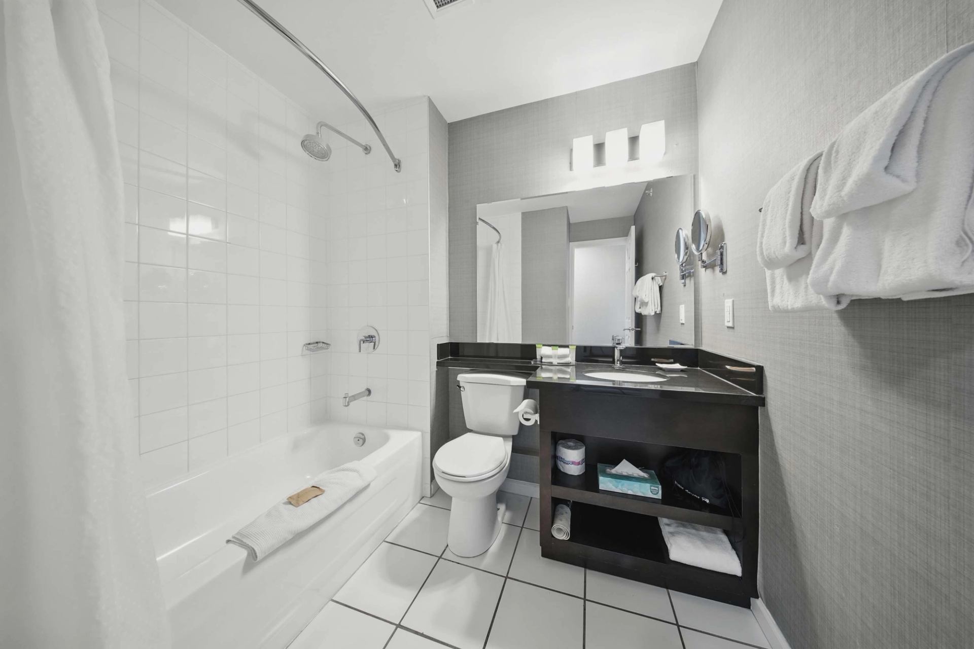 Modern bathroom with bathtub, toilet, black vanity, large mirror and folded towels.